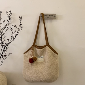 Chic cream fleece tote bag with brown trim and plush pompom hanging on a white wall