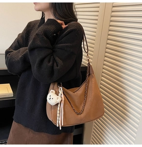 Brown leather moon bag with metal chain, bear charm and woven tassel detail on model