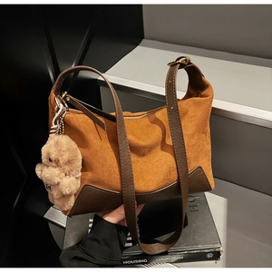 Details einer braunen Wildleder-Tragetasche mit Lederkanten und Teddybär-Anhänger