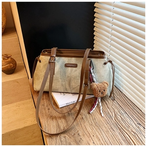 Détail d'un sac d'épaule en daim vert sauge avec bordure en cuir marron et ours peluche