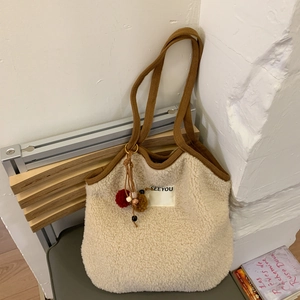 Close-up of plush off-white underarm bag featuring brown straps and fuzzy ball charms