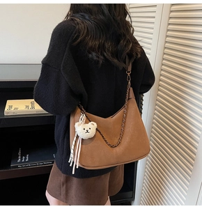 Close-up of brown faux leather shoulder bag with metal chain and plush bear charm