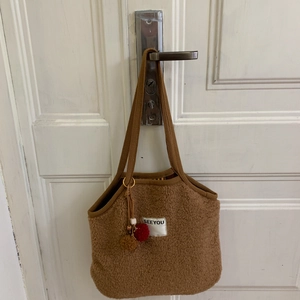 Detail of a brown plush shoulder bag with SEEYOU label and colorful pompom charm