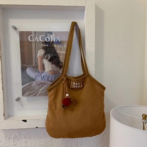 Detail of a brown suede shoulder bag featuring a Bonjour tag and colorful pompom charm