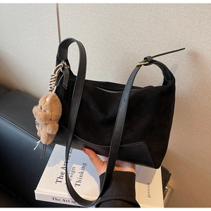 Detailansicht der schwarzen Wildledertasche mit braunem Plüschbären-Anhänger und Gurt