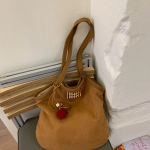 Brown suede tote bag detail with Bonjour text patch and decorative red plush charm