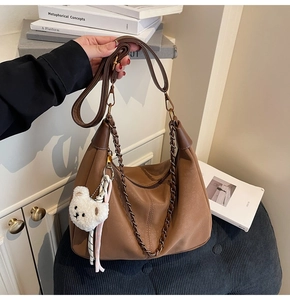 Close-up of brown hobo bag with metal chain strap, leather strap and plush bear charm