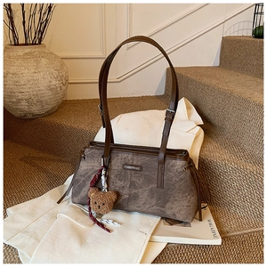 Détail du sac à bandoulière marron vintage avec finition texturée et breloque ours en peluche