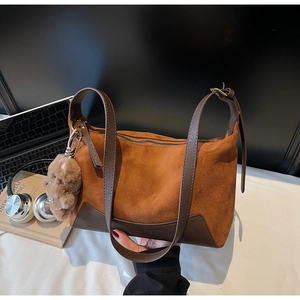 Detail einer braunen Wildledertasche mit Teddybär-Anhänger auf dem Schreibtisch