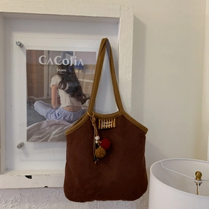 Close-up of brown suede tote bag with Bonjour embroidery and plush ball pendant