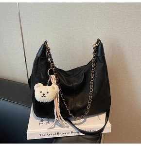 Detail of black leather dumpling bag with metal chain and plush bear charm on books