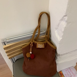 Brown corduroy shoulder bag with Bonjour label and plush ball detail in cozy setting