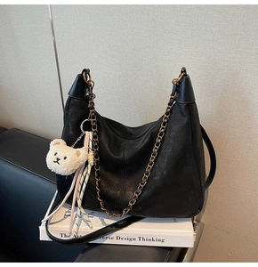 Close-up of black leather hobo bag with gold chain and teddy bear charm on a book