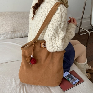 Detail of brown suede shoulder bag with BonBon fabric tag and plush charm accessory