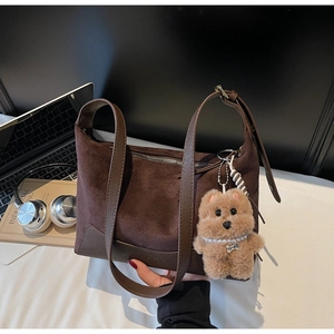 Braune Wildleder-Hobo-Tasche im Detail mit Plüschbären-Anhänger und Lederriemen am Tisch