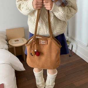 Close-up of brown canvas shoulder bag featuring Bonjour embroidery and pompom charm