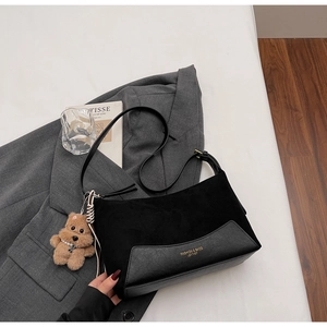 Detail der schwarzen Wildleder-Tasche mit Lederbesatz und braunem Plüschbären-Anhänger