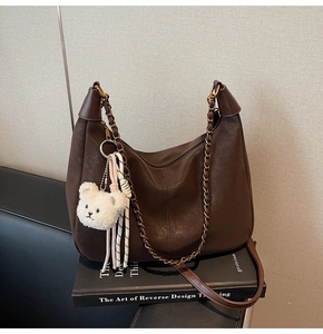 Detailed close-up of deep brown pebbled leather bag with plush bear charm and chain strap