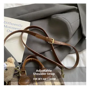 Detail of adjustable leather strap with gold buckle and plush bear charm on brown bag