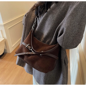 Détail d'un sac bandoulière en daim marron foncé avec œillets argentés et bandoulière cuir