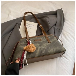 Détail du sac bandoulière vert délavé avec pendentif ours en peluche et plaque en métal