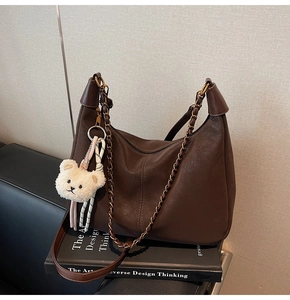 Detail of dark brown leather handbag featuring a white teddy bear charm and metal chain strap