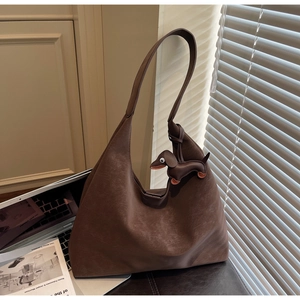 Deep brown matte hobo shoulder bag with a dog charm and laptop in a cozy office setting
