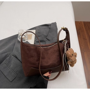 Detailansicht der braunen Wildledertasche mit Plüschbären-Anhänger auf weißem Grund