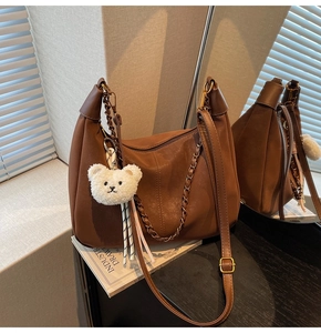 Brown leather hobo bag with chain detail, plush bear charm, and adjustable strap