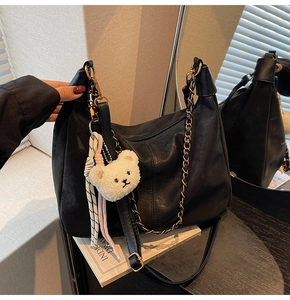 Detail of black matte leather hobo bag with V-shaped opening and cute bear pendant