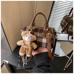 Close-up of retro plaid wool handbag with brown leather straps and a cute teddy bear charm