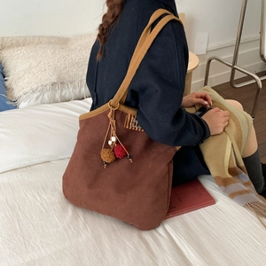 Brown suede tote bag with yellow woven straps and decorative pompom on a bed