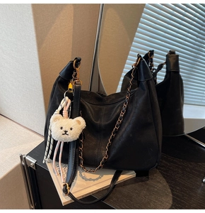 Detail of black large hobo bag with metal chain strap and white plush bear pendant