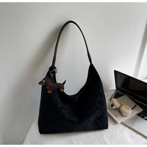 Detail of black matte suede hobo bag with a brown dachshund charm in a lifestyle office setting
