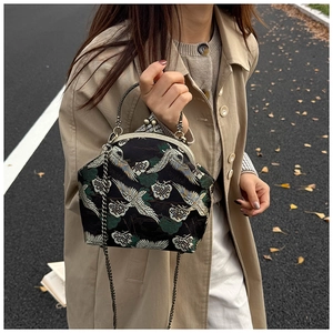 Close-up of vintage embroidery bag with crane pattern and metal chain in autumn setting