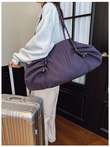 Gros plan d'un grand sac cabas plissé violet avec des anses en corde devant une valise argentée