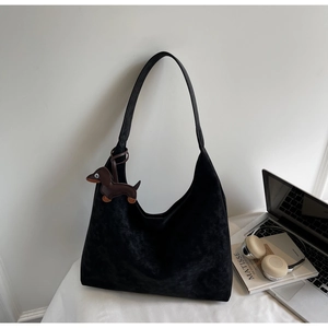 Close-up of minimalist black suede tote bag with a brown dachshund charm on a desk