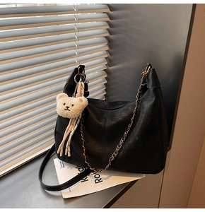 Detail of black matte leather bag with retro chain and plush bear charm in window light
