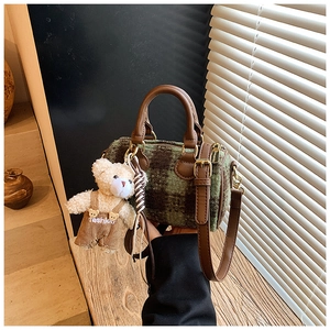 Detail of wool plaid barrel bag featuring brown leather handles and teddy bear charm