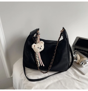 Detail of matte black hobo bag with vintage copper chain and white bear plush charm