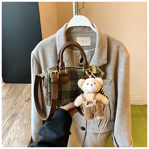 Detail of green plaid wool boston bag with brown leather handles and bear charm