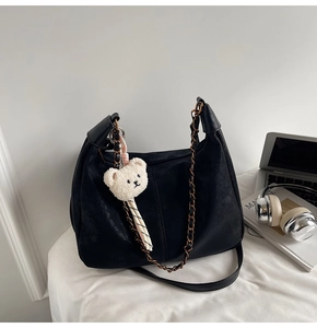 Detail of black matte leather tote bag with gold chain strap and cute bear charm