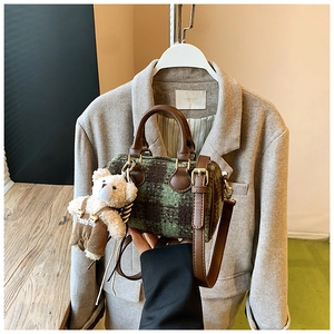 Detail of green plaid barrel bag with brown leather handles and a teddy bear charm