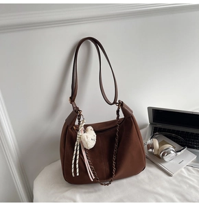 Detail of dark brown leather hobo bag with gold chain and plush bear charm