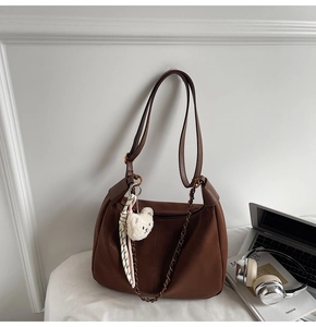 Brown faux leather dumpling bag detail with plush bear charm and decorative silk scarf