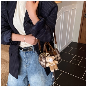 Close-up of a brown checkered cylinder bag with a cute plush bear charm on a model