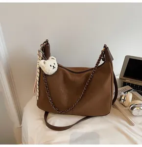 Detail of dark brown Hobo bag with plush bear charm, striped scarf and bronze chain strap