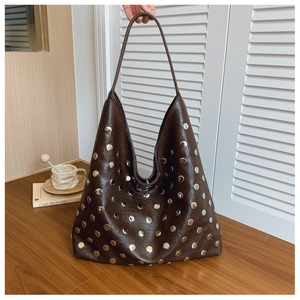 Detail of dark brown leather tote bag with silver metal rivets on a wooden table