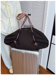 Détail du sac cabas plissé noir avec anses en corde tressée sur une valise argentée