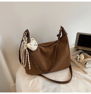Brown hobo bag detail with plush bear charm and chain on a white aesthetic background